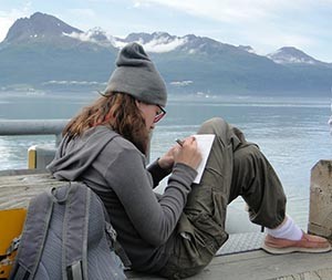 Copper River Stewardship Expeditioner writes a journal entry. Valdez Marine Terminal in the background.