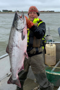Gordon Terpening stands on a fishing boat, holding up a large salmon.