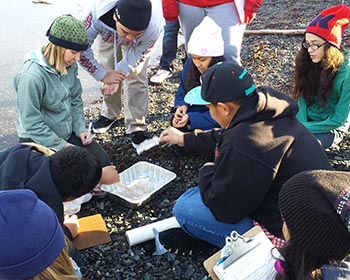 Curriculum creator Katie Gavenus (green hat at left) shows Whittier students how oiled water affects bird feathers. Photo by Lisa Matlock.